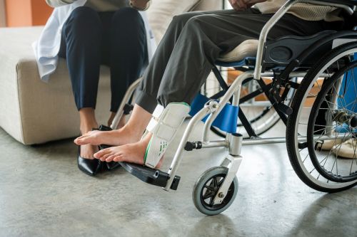 Injured woman broken ankle wearing ankle support on wheelchair at the hospital after personal injury accident.