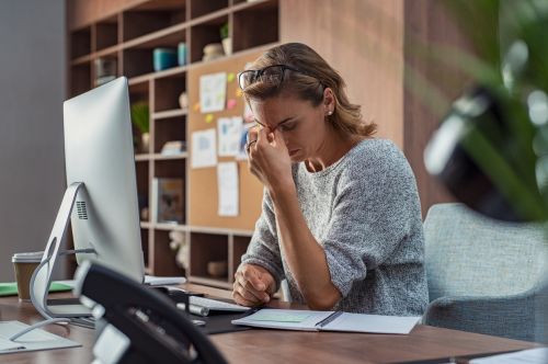 Woman at an office desk with spectacles on head feeling emotional distress about her situation.